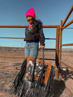 a woman holding a fringe bag in front of a fence