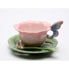 a pink tea cup and saucer sitting on top of a green leafy plate