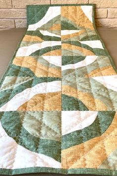 a quilted table runner with green and yellow circles on it, sitting against a brick wall