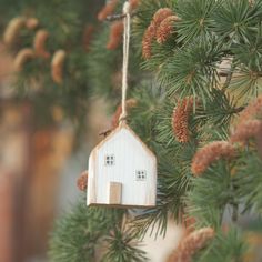 a wooden house ornament hanging from a pine tree with cones on the branches