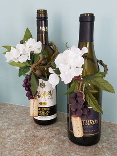 two bottles of wine with flowers and leaves in them on a counter top next to each other