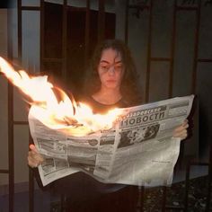 a woman holding a newspaper with flames coming out of it