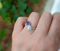 a person's hand holding a ring with an amethorate and pearl