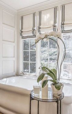 a bath tub sitting next to a window filled with white flowers and plants in vases