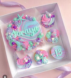 a box filled with cupcakes covered in frosting and colorful icing on top of a table