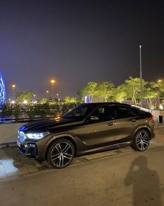 a black car parked in front of a ferris wheel at night with its lights on