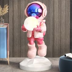 an astronaut statue holding a white object in his right hand and standing next to a blue cabinet