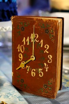 a clock made out of an old book sitting on a table with flowers in the background