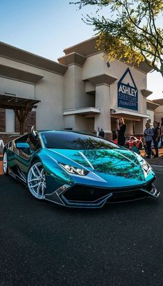 a blue sports car parked in front of a building with people looking at it from the street