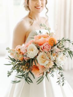 a bride holding a bouquet of flowers in her hand and smiling at the camera while standing next to a window