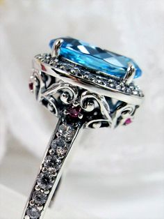 Natural Blue Topaz Sterling Silver RingHalo Design #D228 If you have a penchant for classic vintage jewelry, then this beautiful natural blue topaz Halo Ring #D228 is just the thing for you. Crafted with love in sterling silver filigree and a magnificent centerpiece – an 11x9mm natural blue topaz gemstone – this ring is sure to become your favorite piece of jewelry. With all the amazing & intricate details plus the lovely oval center stone, this Art Deco design will surely turn heads and get att Antique Blue Multi-stone Jewelry, Elegant Sapphire Multi-stone Topaz Ring, Vintage Topaz Ring With Accent Stones Gift, Vintage Blue Multi-stone Ring, Vintage Blue Topaz Ring With Accent Stones, Antique Blue Topaz Ring With Center Stone, Elegant Multi-stone Topaz Ring As A Gift, Elegant Multi-stone Topaz Ring For Gift, Vintage Blue Halo Setting Jewelry