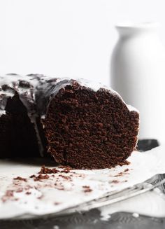 a piece of chocolate cake on a plate next to a white vase and silverware