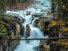 a bridge over a river that is surrounded by trees and rocks with water running down it