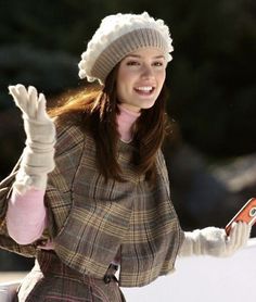 a woman in plaid coat and hat holding an orange cell phone while standing on snow covered ground