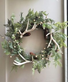 a wreath with antlers, pine cones and greenery hanging on a wall next to a window