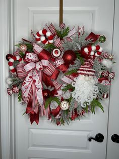 a christmas wreath is hanging on the front door with ornaments around it and decorations in red, white and silver