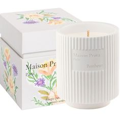 a white candle sitting next to a box on a white surface with flowers painted all over it