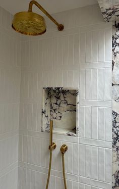 a bathroom with white tile, gold fixtures and a marbled shower head in the corner