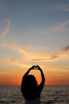 a woman making a heart shape with her hands on the beach at sunset or sunrise