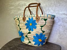 a basket with blue flowers painted on it sitting on a wooden table next to a wall