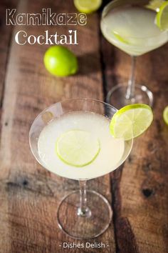 two glasses filled with drinks sitting on top of a wooden table next to limes