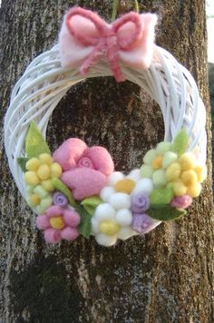 a white wreath with pink and yellow flowers hanging from it's side next to a tree