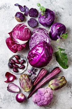 an assortment of purple vegetables on a white surface with green leaves and red cabbages