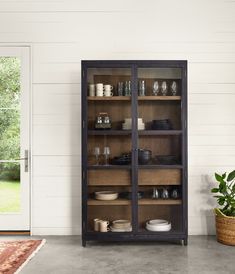 an open bookcase with glass doors on the front and side, next to a potted plant