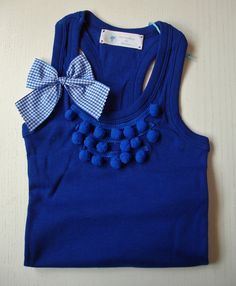 a blue tank top with a bow and pom - poms on the front