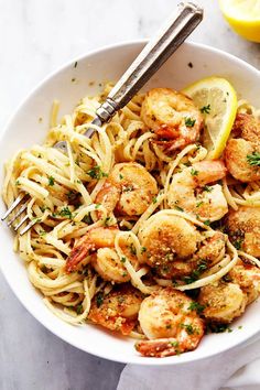 a white bowl filled with shrimp and pasta next to lemon wedges on a table