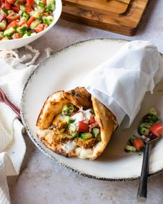 a burrito on a plate next to a bowl of salad and a serving utensil