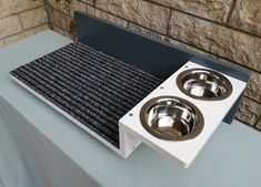 two stainless steel dog bowls on top of a blue table with a stone wall in the background