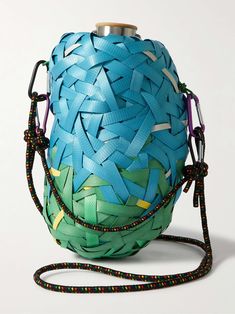 a blue and green woven bag with a metal top on a white surface, tied to a string