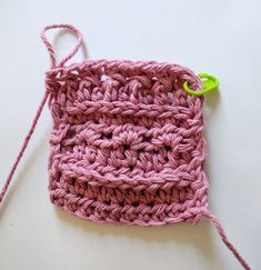 a pink crochet bag with a green hook on it's end sitting on a white surface