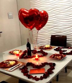 two heart shaped balloons sitting on top of a table next to plates with food and candles