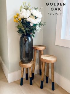 two wooden stools with flowers in them next to a vase on the floor and wall