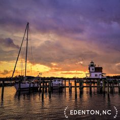 boats are docked in the water near a light house at sunset with clouds above them