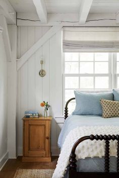 a bed sitting under a window next to a wooden dresser in a white walled room