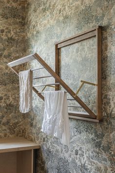 clothes hanging on a rack in front of a mirror and wallpapered wall with floral designs