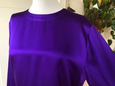 "Vintage 1980s-90's 100% silk satin blouse in a deep purple. Missing tags but is without a doubt 100% silk. Size is unknown but estimated to be a size S or possibly M. Please allow for extra room as blouse goes over the head. Single button at back of neck with keyhole closure, and matching buttons at cuffs. Boxy bodice with long sleeved that are puffed/gathered at cuffs. In AS IS condition; the silk has areas of \"stress\" or \"stretch mark\" type areas near armpits and at front, also has a fain Purple Silk Evening Top, Purple Silk Evening Blouse, Purple Silk Formal Blouse, Formal Purple Silk Blouse, Purple Silk Top For Formal Occasions, Formal Purple Silk Top, Purple Silk Party Tops, Purple Satin Party Top, 40s Hollywood