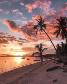 the sun is setting on a tropical beach with palm trees and boats in the water