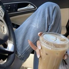 a woman holding a cup of coffee while sitting in the driver's seat of a car