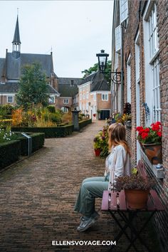 a woman sitting on top of a bench next to a brick building and flower pots