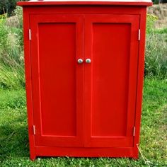 a red cabinet sitting on top of a lush green field