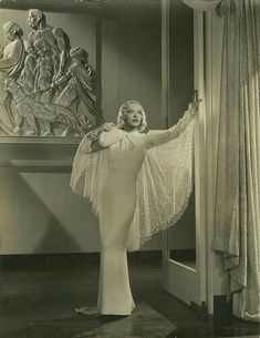 an old photo of a woman standing in front of a statue with her arms outstretched