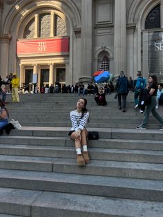 a woman sitting on the steps in front of a building with people walking around it