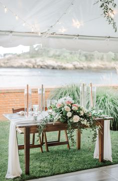 a table with flowers and candles is set up for an outdoor wedding reception by the water