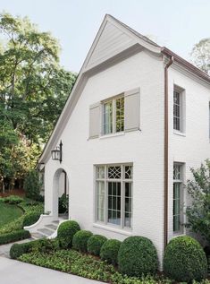 a white house with hedges in front of it and bushes around the windows on either side