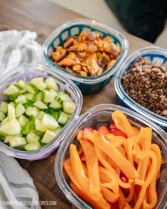 four plastic containers filled with different types of food on top of a wooden table next to a towel