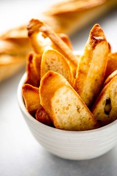 a white bowl filled with french fries sitting on top of a table next to breadsticks